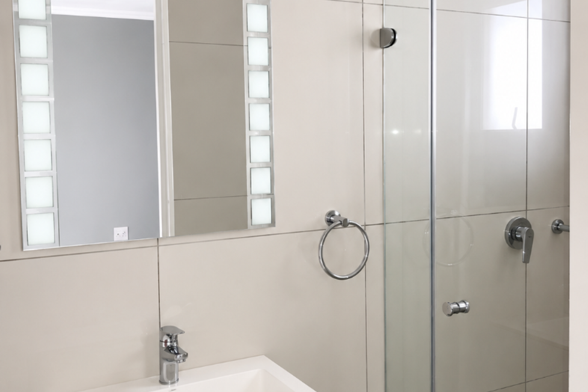 Modern bathroom featuring a sleek vanity with basin, illuminated mirror, and a glass-enclosed shower with contemporary wall tiling.