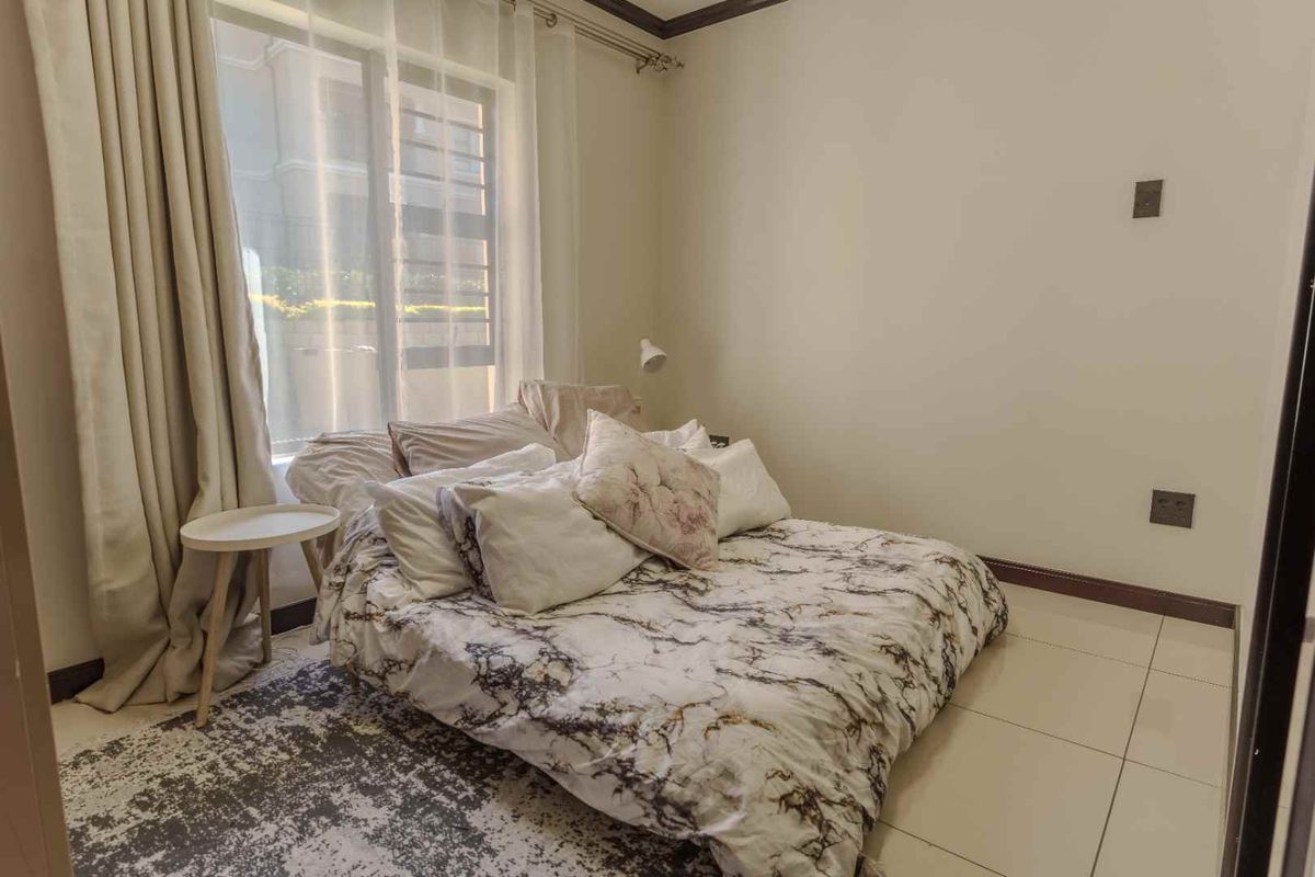 A well-lit bedroom featuring neutral tiled flooring, dark skirting boards, and a large window with curtain tracks.