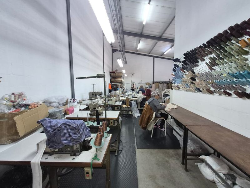 Industrial workshop space featuring exposed steel roof trusses, fluorescent lighting, concrete flooring, and extensive wall-mounted storage for thread spools.