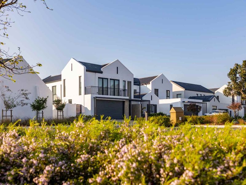 A modern residential exterior featuring white facades, dark metal roofing, and integrated garages within a well-maintained estate setting.