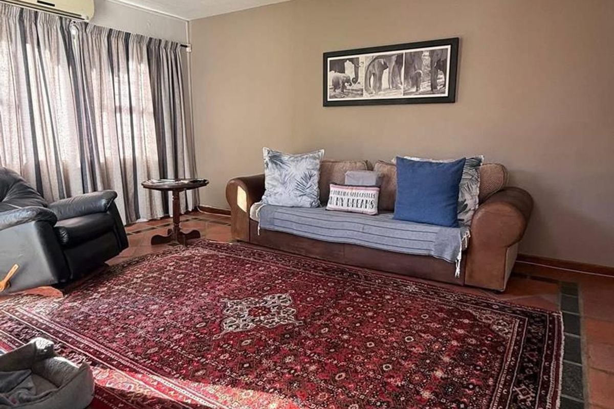 A living room featuring terracotta floor tiles, a wall-mounted air conditioning unit, and large windows with curtains.