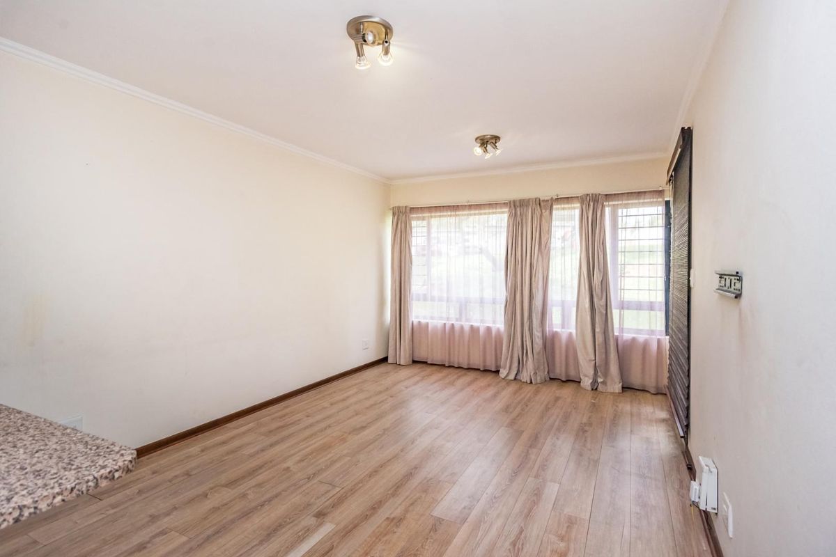 A bright, empty living area featuring wood-look laminate flooring, large windows with curtain tracks, and dual ceiling-mounted light fixtures.
