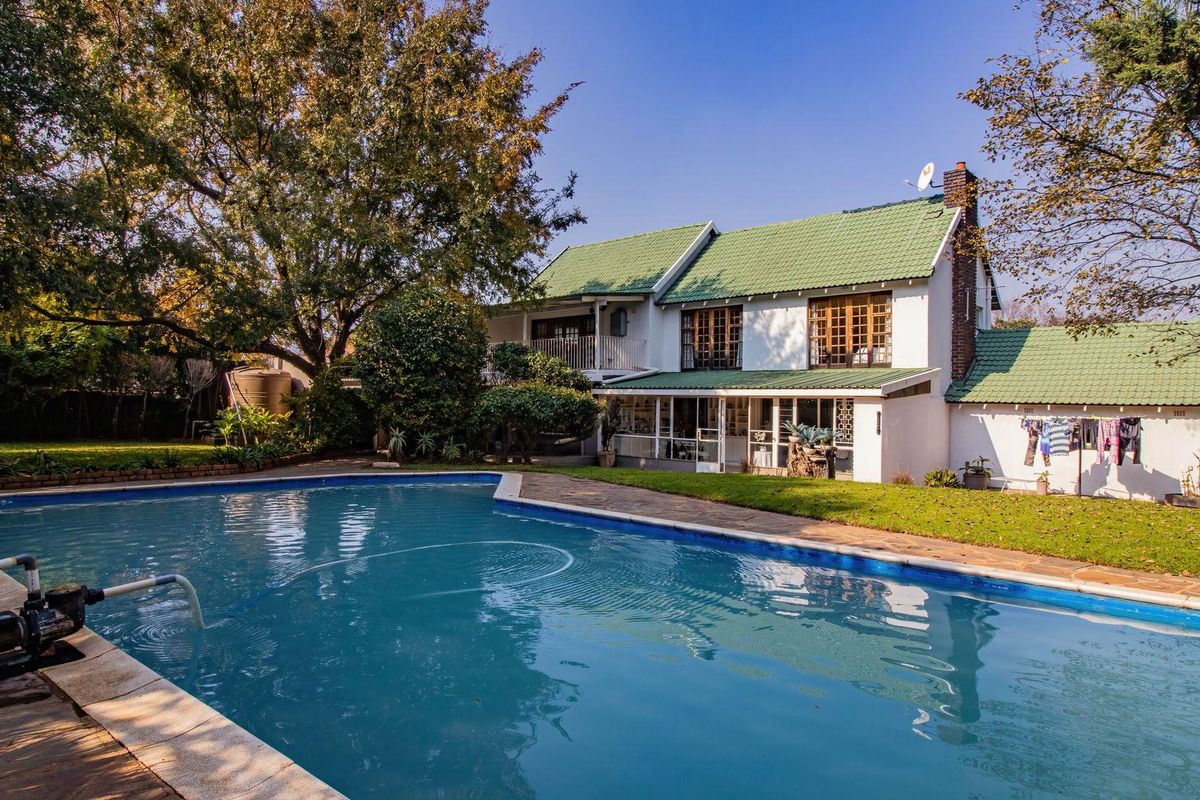 A spacious rear garden featuring a large swimming pool, established trees, and a two-story house with a green tiled roof and patio area.