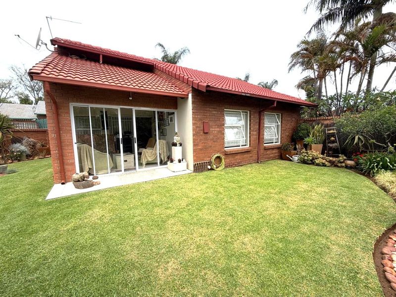 Rear view of a brick house featuring a tiled roof, sliding glass doors, and a well-maintained garden area.