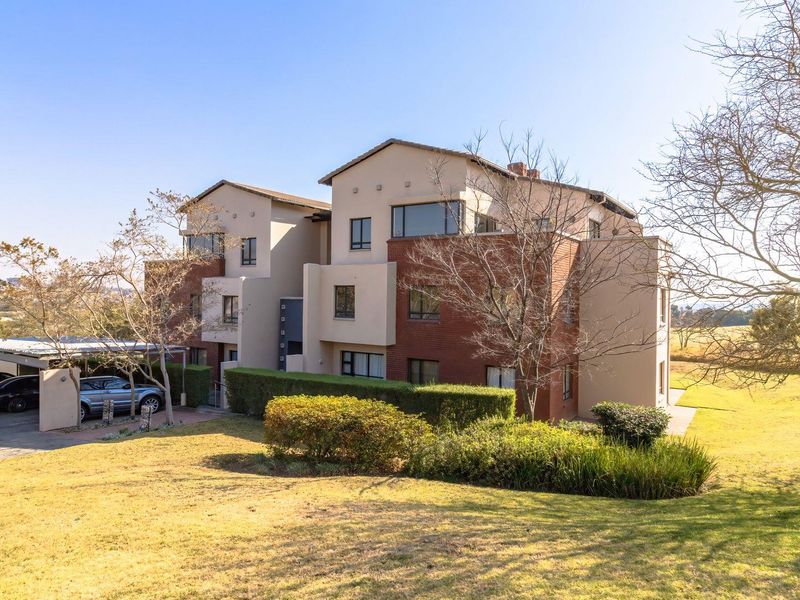 A multi-story apartment building featuring a combination of brick and plastered exterior finishes, complete with a covered carport and surrounding landscaped grounds.