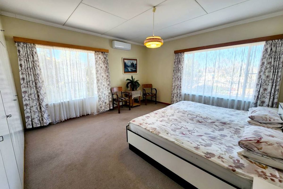 Spacious bedroom featuring large windows, built-in cupboards, and a wall-mounted air conditioning unit.