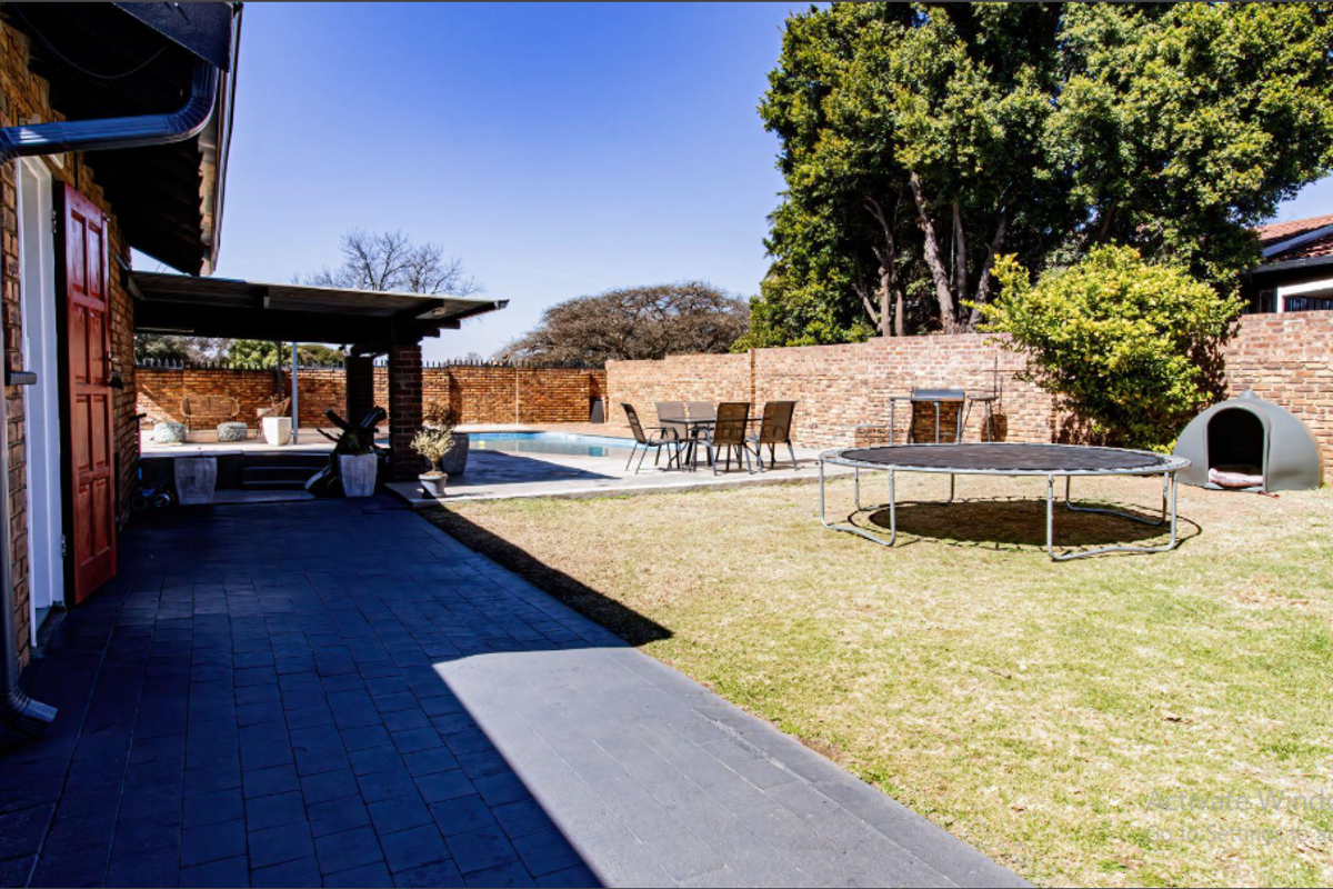 A spacious rear garden featuring a swimming pool, a covered patio area, and a brick boundary wall, providing a private outdoor entertainment space.
