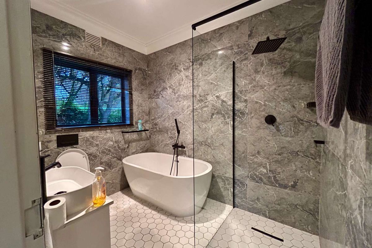 Modern bathroom featuring a freestanding bathtub, a walk-in shower with a glass screen, and elegant grey marble-style wall tiling with hexagonal floor tiles.