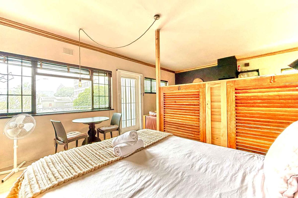 A bedroom featuring a louvered wooden room divider, large windows providing natural light, and access to an exterior area via a glass panel door.