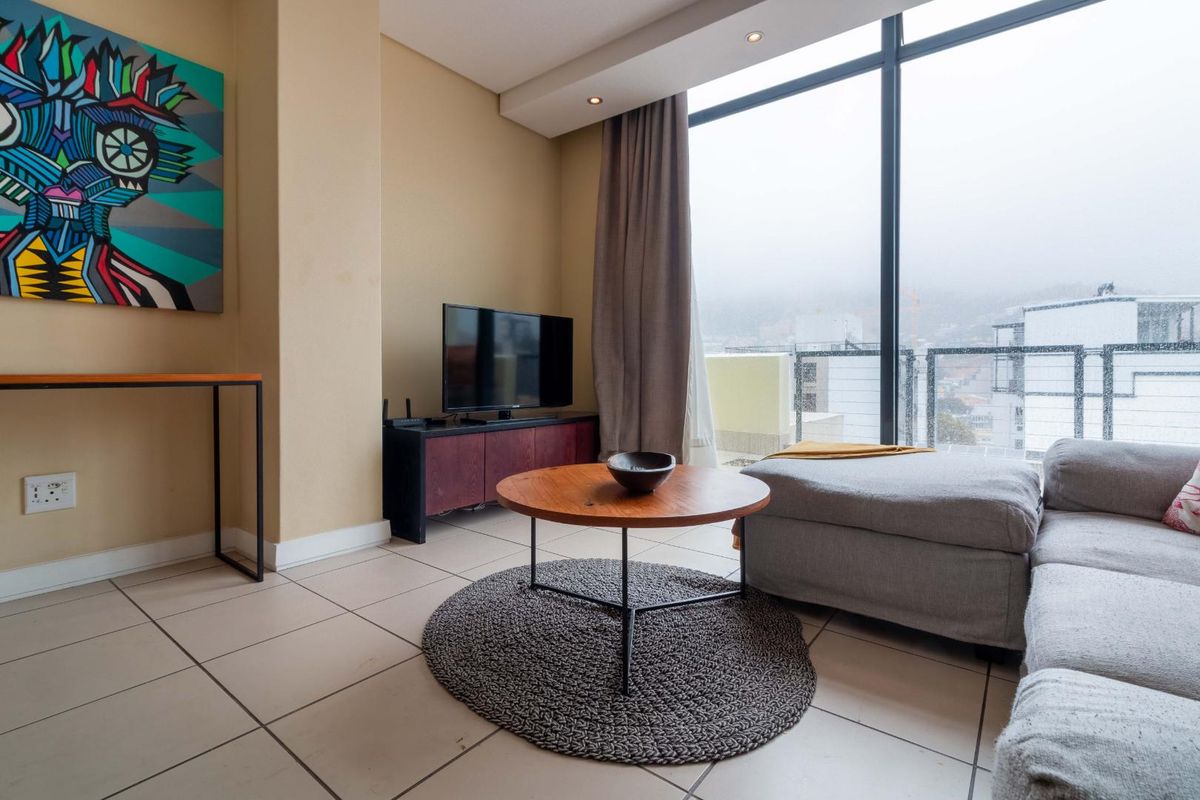A bright living room featuring large floor-to-ceiling windows with balcony access, neutral tiled flooring, and recessed ceiling lighting.