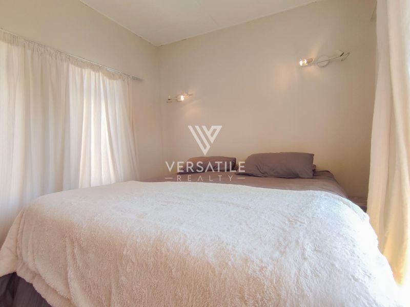 A neutrally decorated bedroom featuring wall-mounted lighting and window treatments.
