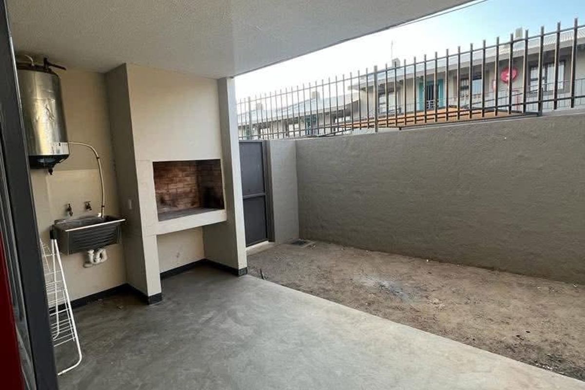 Covered patio area featuring a built-in braai, stainless steel sink, and an adjacent open garden space with perimeter security fencing.