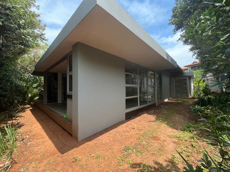 Rear view of the townhouse featuring modern architectural lines, large glass sliding doors, and timber decking set within a natural garden surround.