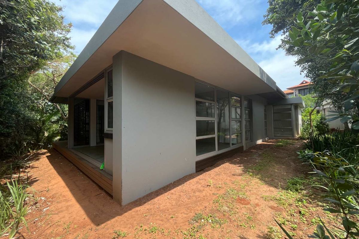 Rear view of the townhouse featuring modern architectural lines, large glass sliding doors, and timber decking set within a natural garden surround.