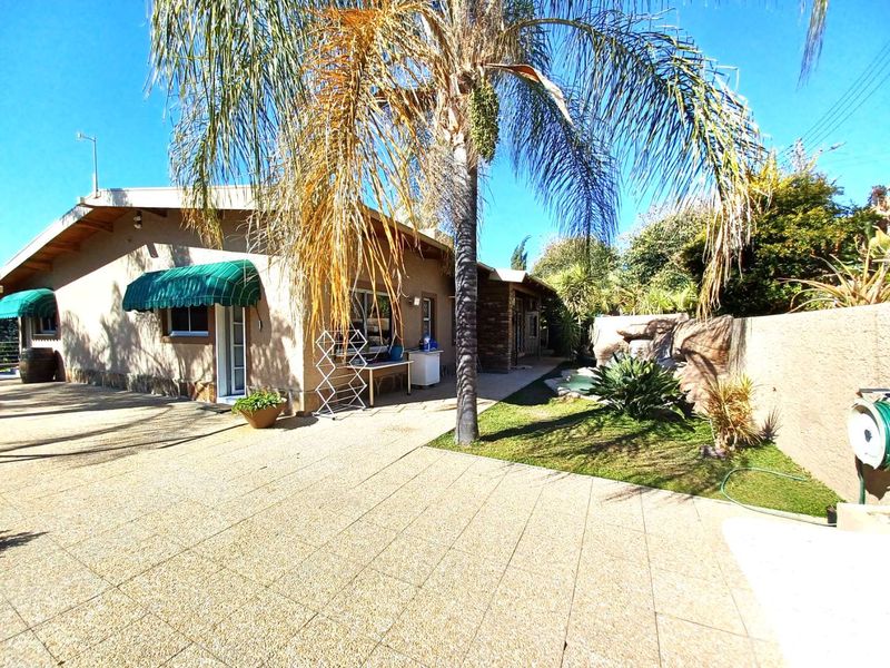 Rear exterior view of the house featuring a paved patio area, established palm tree, and a built-in rock water feature in the garden.