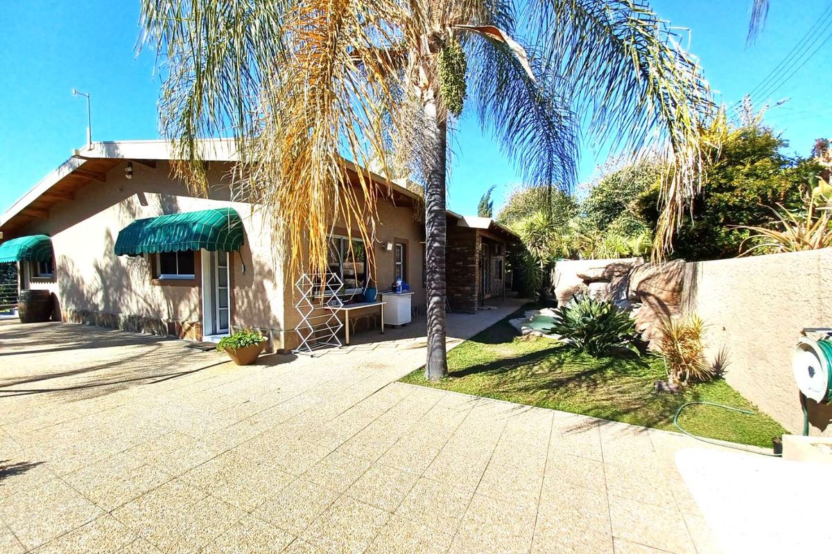 Rear exterior view of the house featuring a paved patio area, established palm tree, and a built-in rock water feature in the garden.