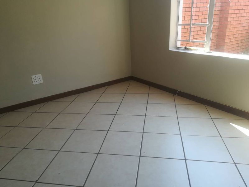 An empty bedroom featuring neutral tiled flooring, skirting boards, and a window fitted with security burglar bars.
