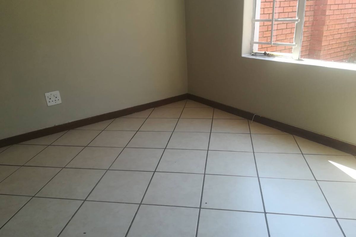 An empty bedroom featuring neutral tiled flooring, skirting boards, and a window fitted with security burglar bars.