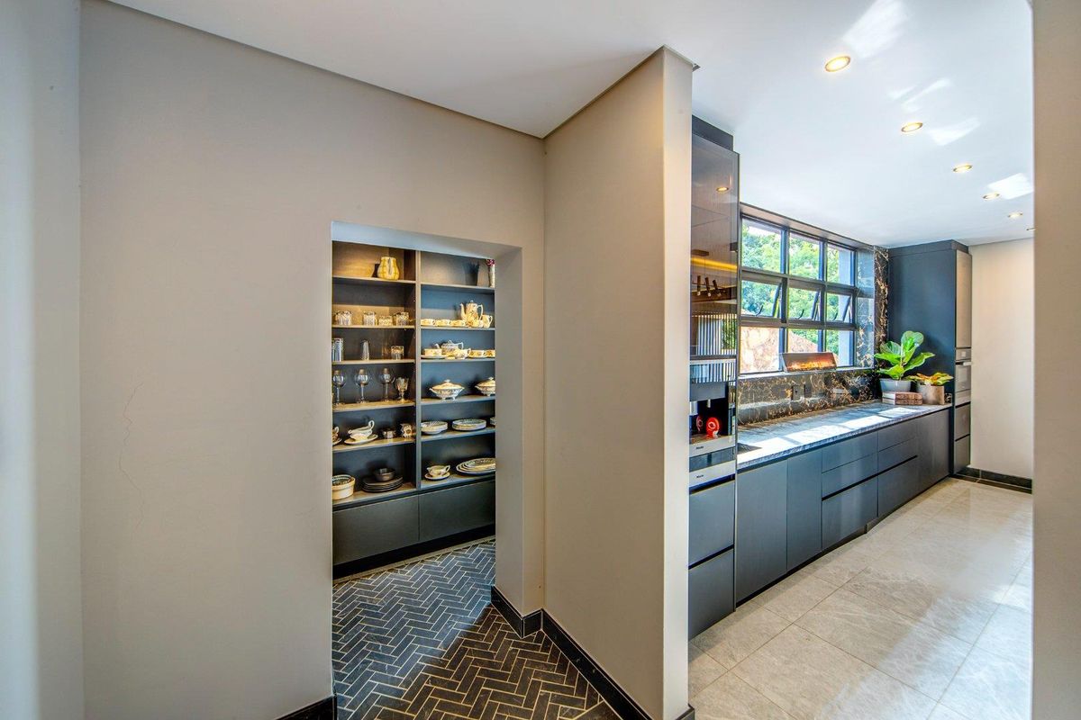 Modern kitchen featuring dark cabinetry, stone countertops, and a dedicated walk-in scullery with custom shelving and herringbone tiled flooring.