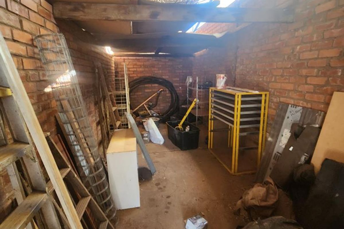 A utilitarian storage or workshop area featuring exposed brick walls and a corrugated metal roof structure.