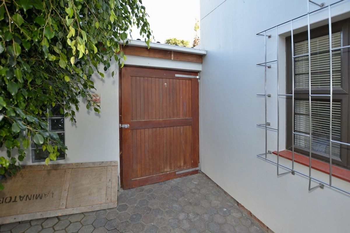 A side exterior area featuring a timber door, paved flooring, and a window with security bars.