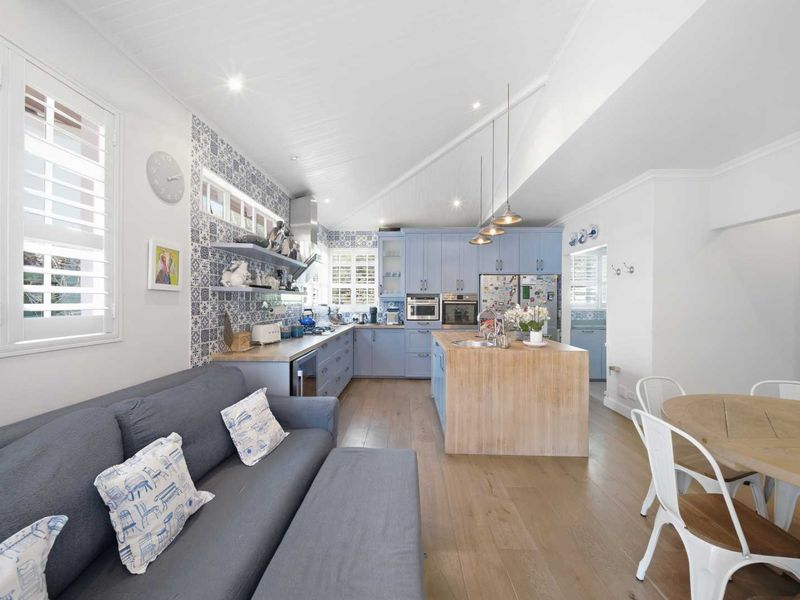 Spacious open-plan kitchen and living area featuring light blue cabinetry, a central timber island, patterned tile splashback, and modern integrated appliances.