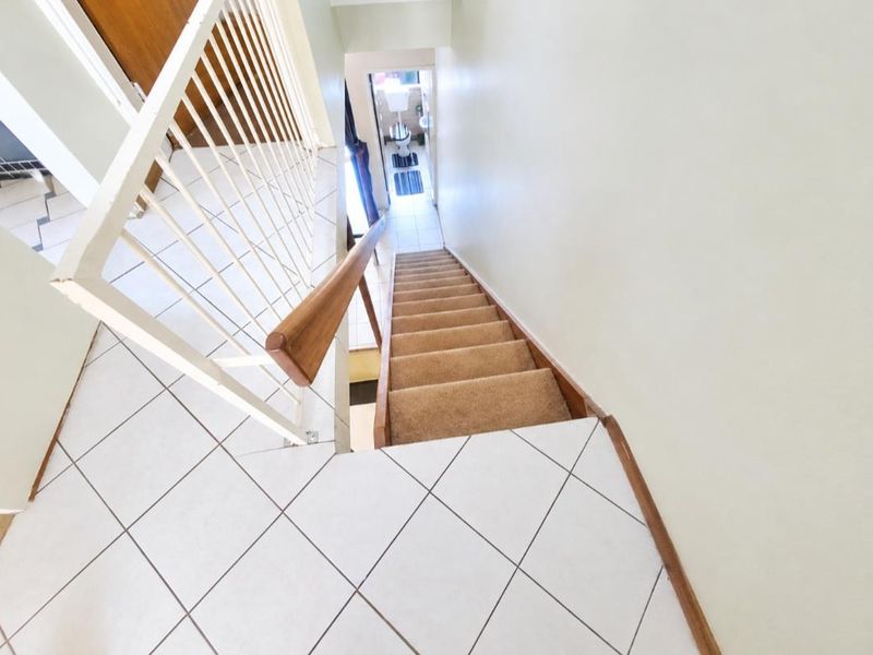 A view looking down a carpeted staircase with a metal balustrade and wooden handrail, leading to a tiled landing area.