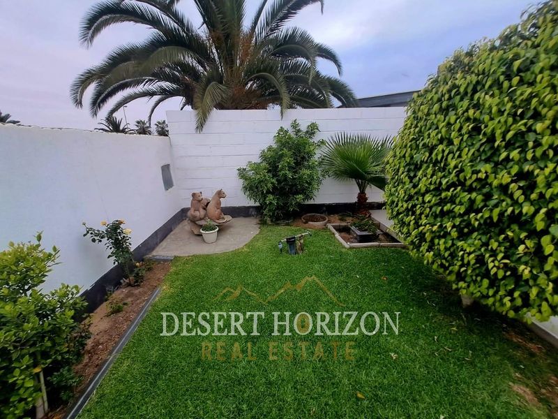 A private garden area featuring a well-maintained lawn, boundary walls, and established palm tree landscaping.
