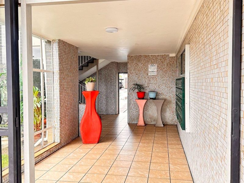 A clean and functional apartment building entrance lobby featuring tiled floors, mosaic wall finishes, and a bank of mailboxes.