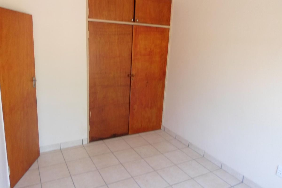 An empty bedroom featuring tiled flooring and built-in wooden cupboards with overhead storage compartments.
