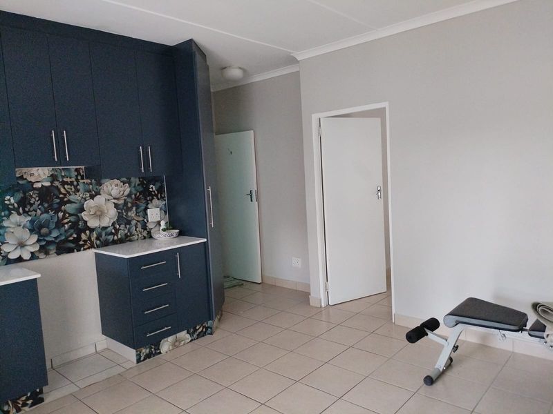 A functional kitchen area featuring modern dark blue cabinetry, a decorative floral backsplash, and neutral tiled flooring, leading into adjacent rooms.