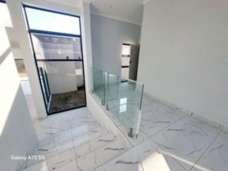 A bright, modern hallway featuring polished marble-look floor tiles and a contemporary glass balustrade overlooking the lower level.