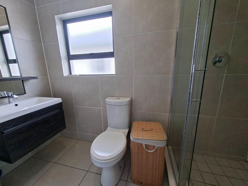 Modern bathroom featuring a vanity cabinet with basin, a toilet, and a glass-enclosed shower with neutral wall and floor tiling.