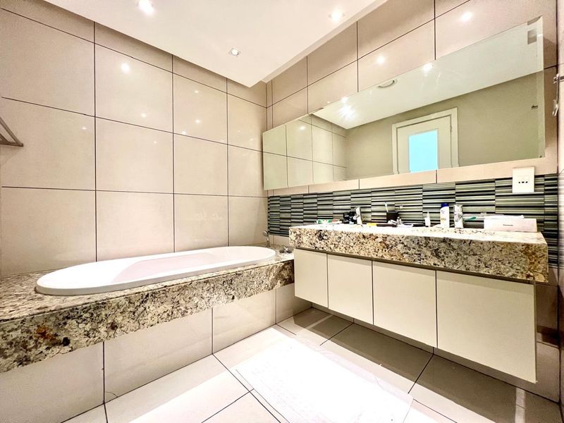 Modern bathroom featuring a built-in bathtub, granite vanity countertop with integrated cabinetry, and large wall-to-wall mirror with recessed lighting.