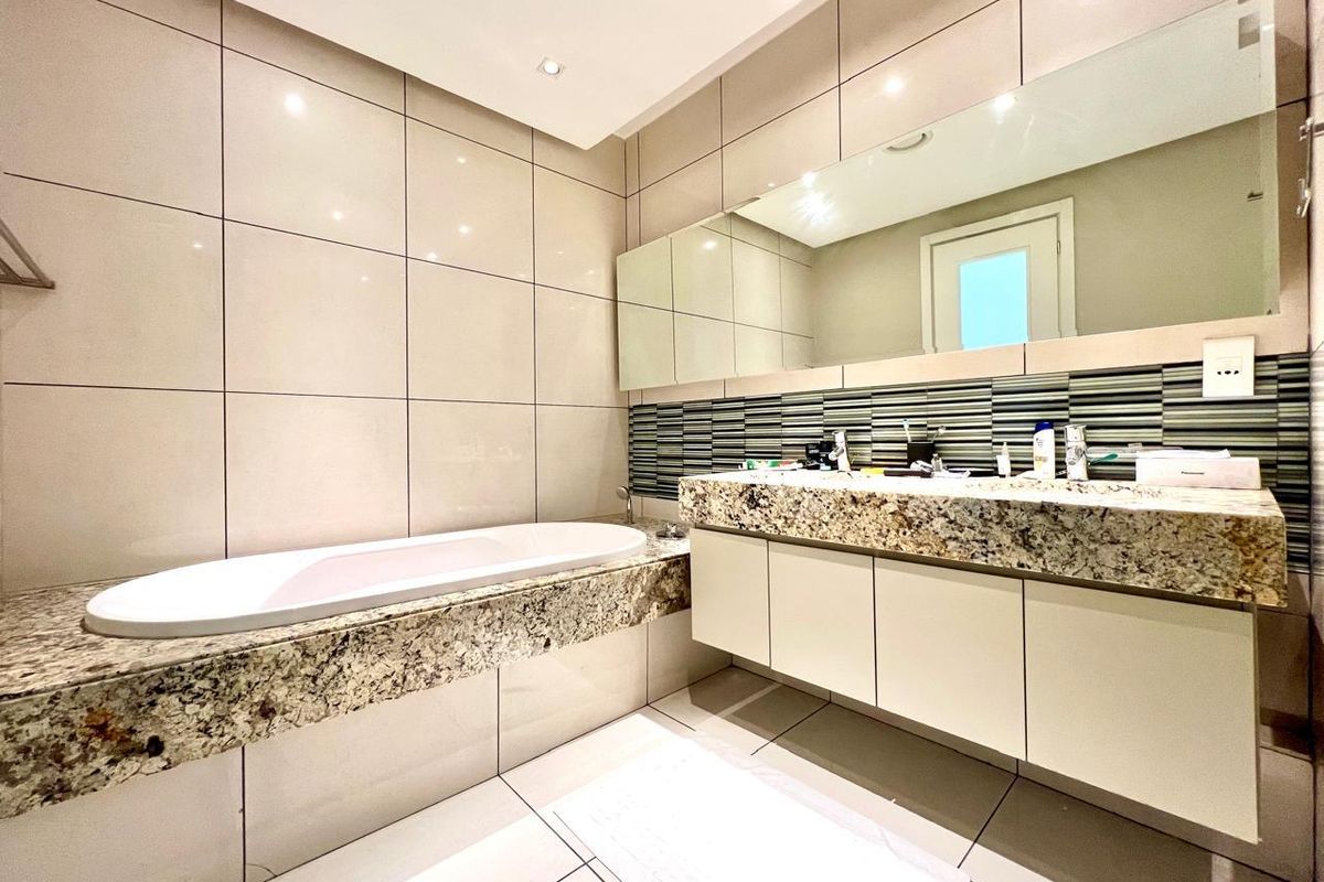 Modern bathroom featuring a built-in bathtub, granite vanity countertop with integrated cabinetry, and large wall-to-wall mirror with recessed lighting.