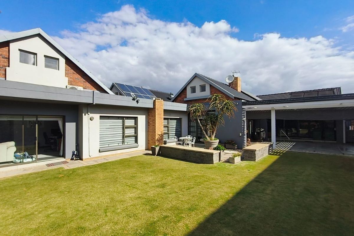 Spacious rear garden featuring a well-maintained lawn, raised brick planters, a covered patio area, and solar panels installed on the roof.