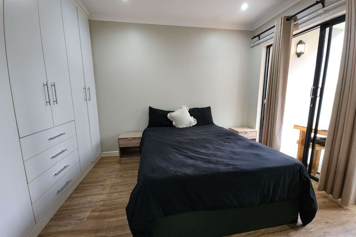 A well-maintained bedroom featuring modern built-in cupboards, laminate flooring, and a sliding glass door providing access to an outdoor area.