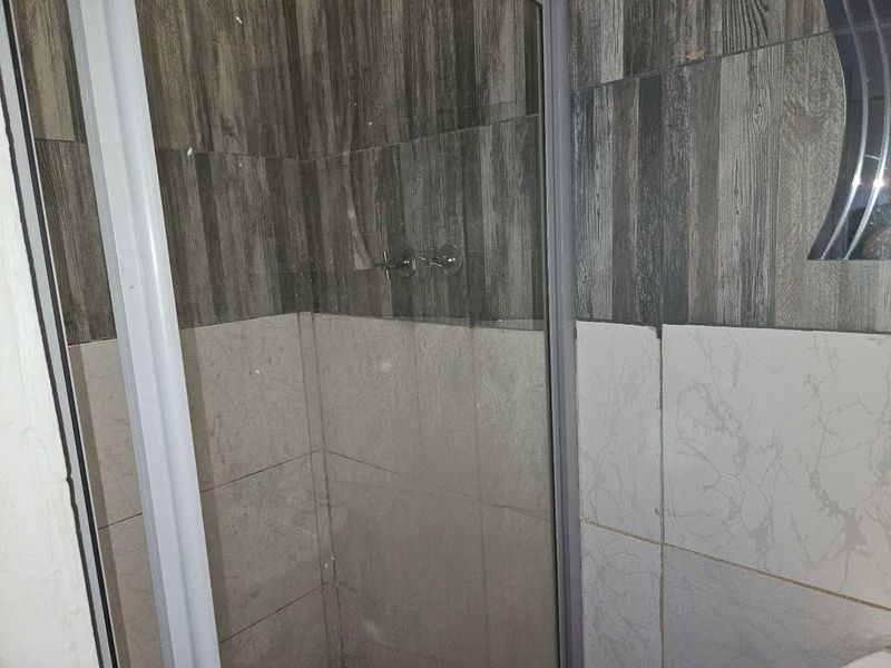 A bathroom shower enclosure featuring mixed wood-look and marble-effect wall tiling with a standard chrome shower mixer.