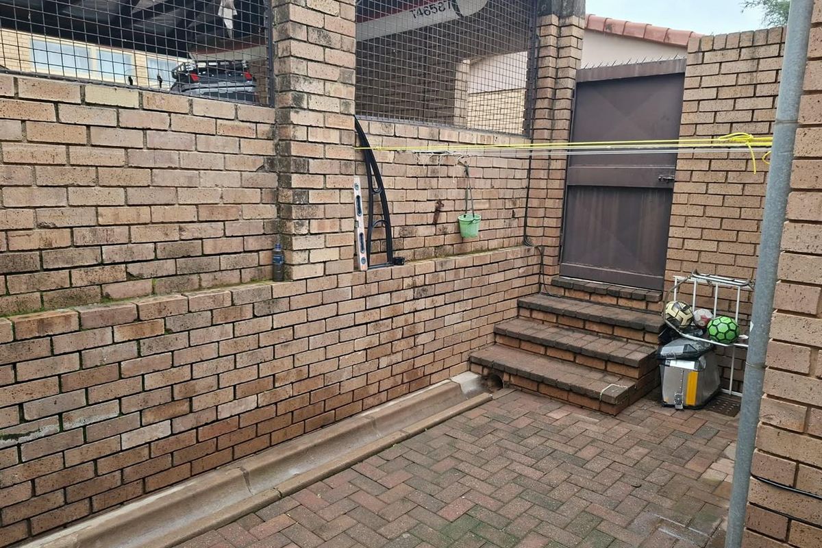 A private rear courtyard featuring brick boundary walls, paved flooring, and concrete steps leading to a secure metal gate.