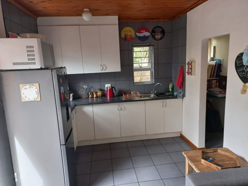 A functional kitchen featuring white cabinetry, dark tiled backsplash, tiled flooring, and a timber ceiling, providing a practical workspace with integrated sink and storage.