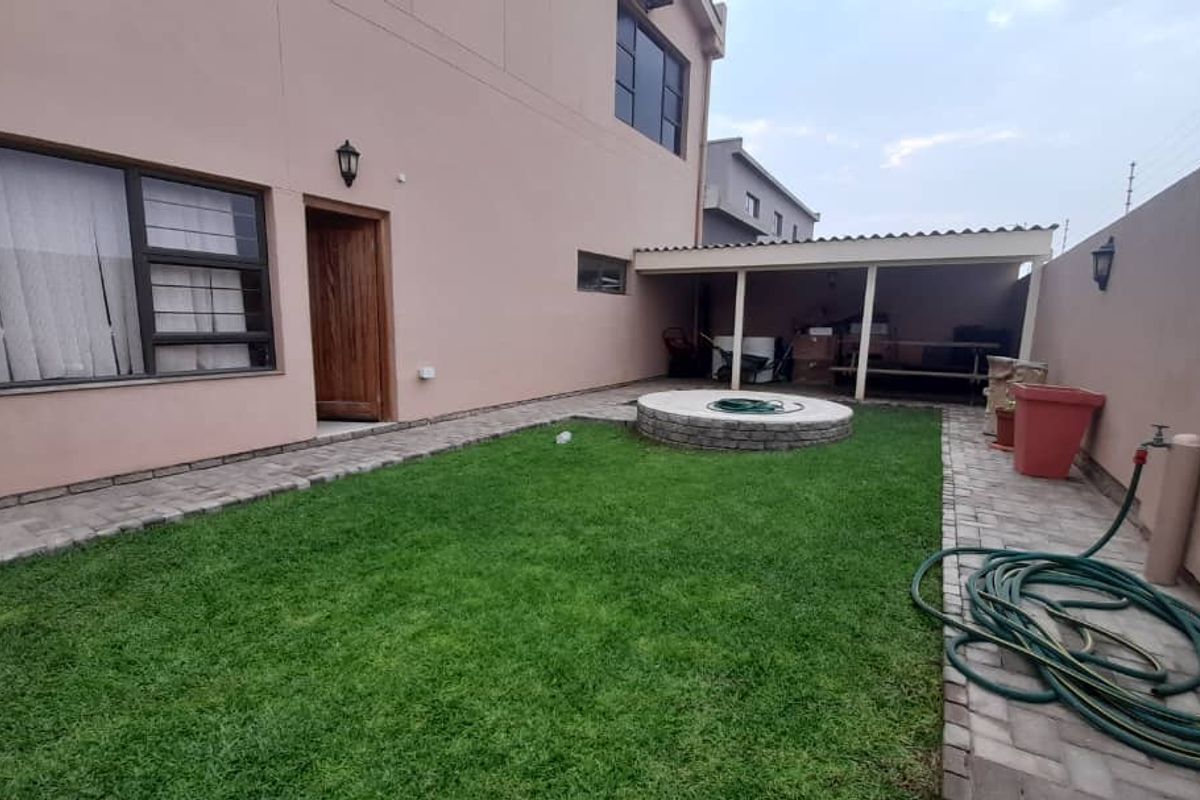 Rear garden area featuring a small lawn, paved pathways, a circular stone feature, and a covered patio area attached to the main dwelling.