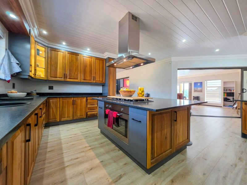 Modern kitchen featuring wooden cabinetry, granite countertops, a central island with built-in oven and cooktop, and a stainless steel extractor fan.