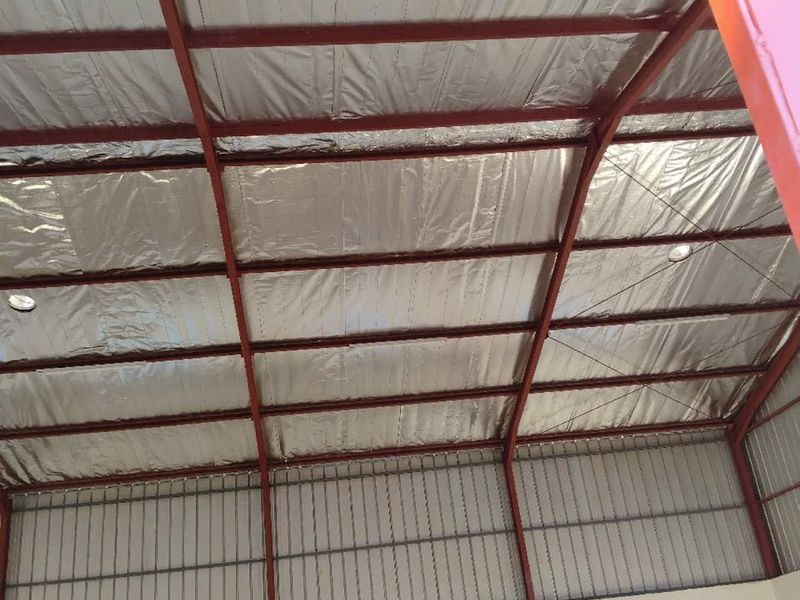 A spacious utility area featuring exposed steel roof trusses, reflective foil insulation, and high-level windows providing natural light.