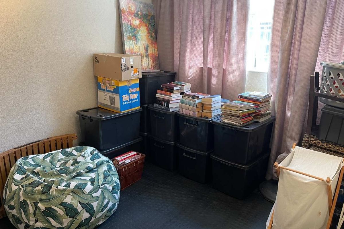 A functional bedroom space featuring dark rubber flooring and large windows with curtains, currently utilized for storage.
