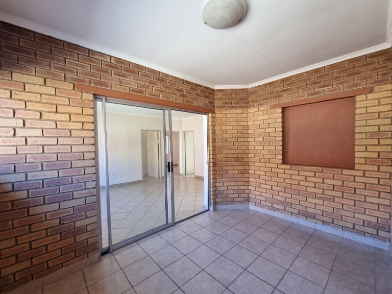 An enclosed patio area featuring exposed brick walls, tiled flooring, and a large sliding glass door leading into the main living space.