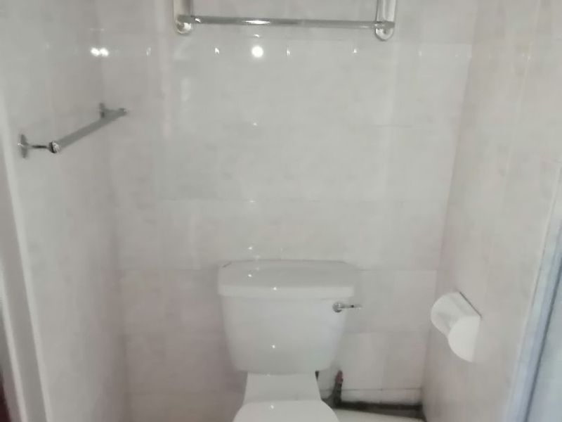 A compact bathroom featuring tiled walls and flooring, equipped with a standard toilet and wall-mounted towel rails.