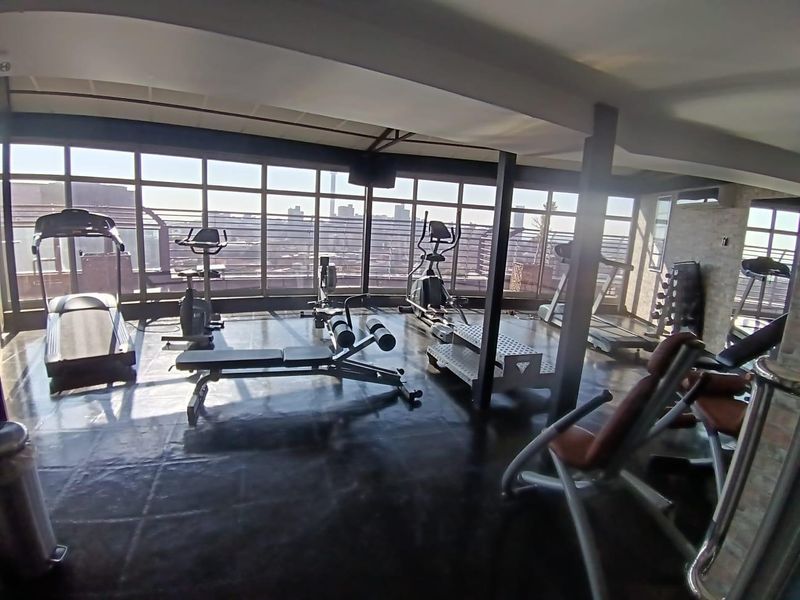A well-lit gym facility featuring large windows with city views, exposed structural beams, and durable flooring.