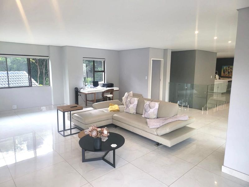 Spacious open-plan living area featuring polished porcelain floor tiles, recessed lighting, and a modern glass balustrade overlooking the lower level.