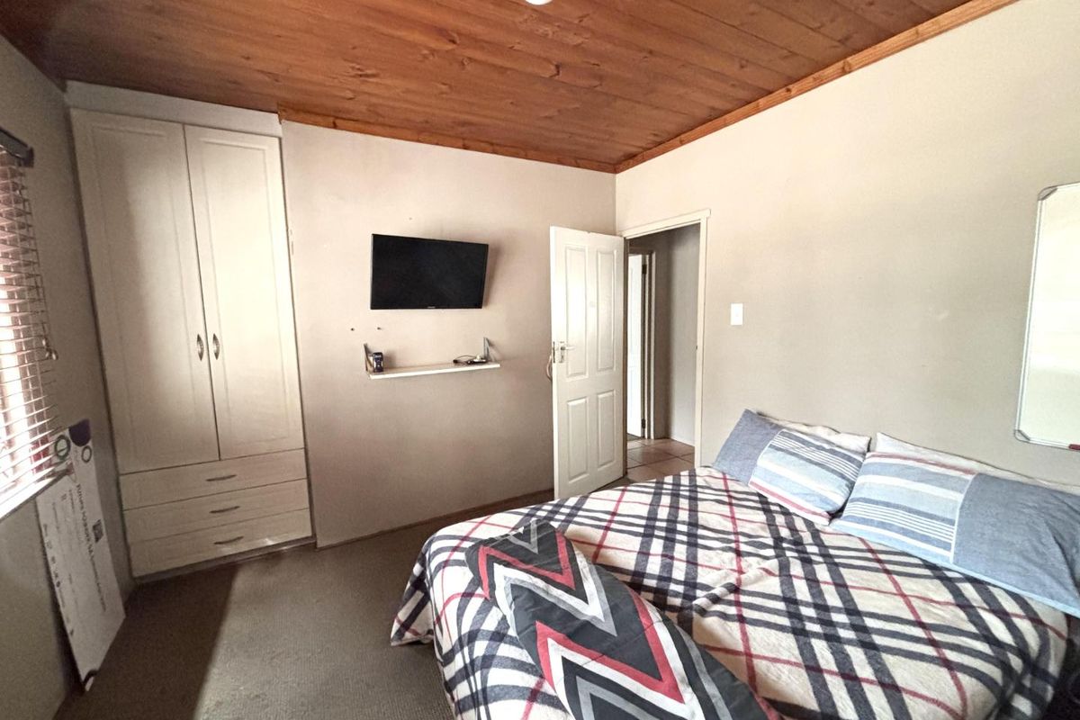 A bedroom featuring a timber ceiling, built-in wardrobe, and carpeted flooring, offering a functional space with potential for modern updates.
