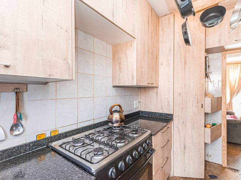 A functional kitchen featuring light wood-look cabinetry, granite countertops, a gas stove, and a built-in pantry cupboard with tiled backsplash.